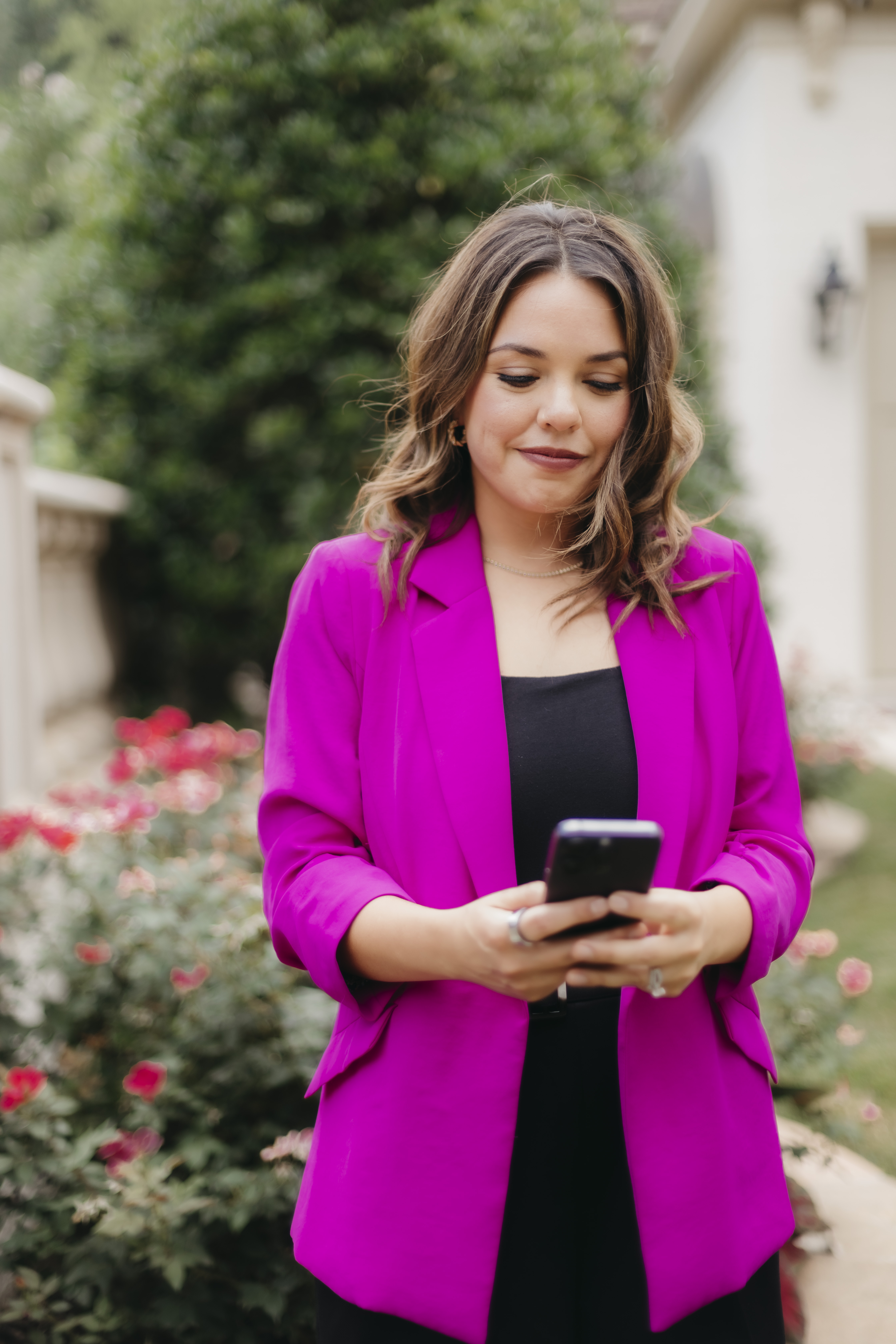 Kristin Wester in a pink blazer looking down at her phone outdoors.